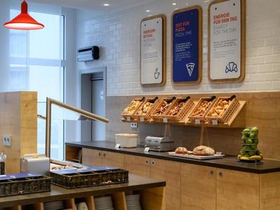 Modernes Café mit Holztheke, Brotauswahl und roter Hängelampe neben großen Fenstern.