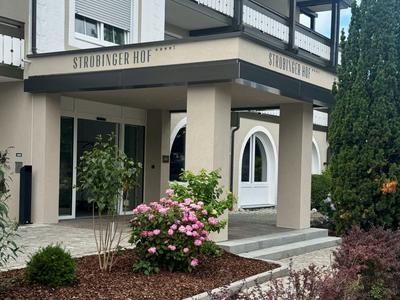 Eingangsbereich eines Hotels mit überdachtem Bereich, Sträuchern und Blumentopf.