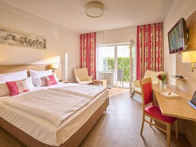 Helles Hotelzimmer mit Doppelbett, Schreibtisch, Sessel und Balkonblick.