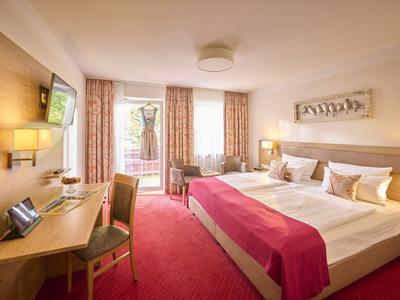 Helles Hotelzimmer mit Doppelbett, Schreibtisch, Sesseln und roten Teppichboden.