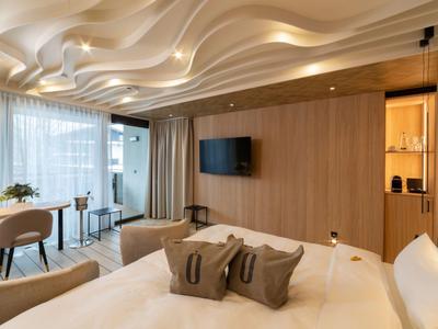 Modernes Hotelzimmer mit Wellen-Decke, Doppelbett und Sitzbereich neben großem Fenster.