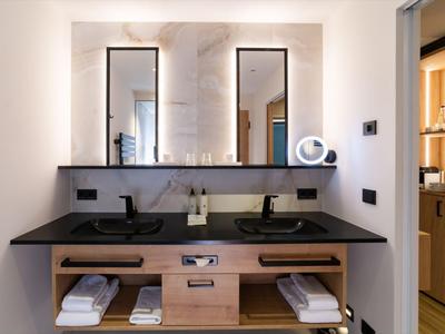 Modernes Badezimmer mit zwei schwarzen Waschbecken, großen Spiegeln und Holzablagen mit Handtüchern.