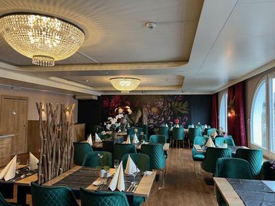 Elegantes Hotelrestaurant mit grünen Sesseln, gedeckten Tischen und Kronleuchtern an der Decke.