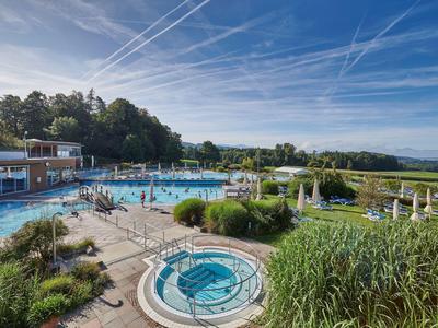 Außenpoolbereich eines Hotels mit Schwimmbecken, Whirlpool und Grünflächen unter blauem Himmel.