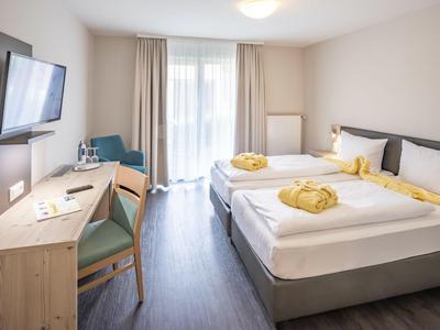 Chambre d'hôtel moderne avec deux lits, bureau, télévision et accès à un balcon.