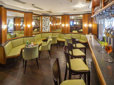 Bar d'hôtel confortable avec sièges vert clair et mobilier en bois sous une lumière chaude.