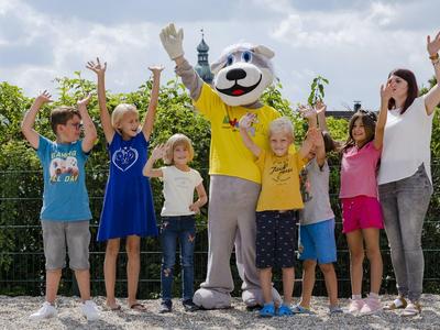 Gruppo di bambini entusiasti e un adulto che posano con una mascotte all'aperto in una giornata soleggiata.