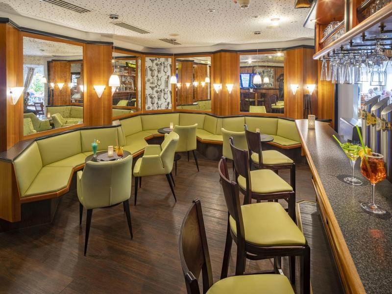 Bar accogliente in hotel con accenti in legno, sedie verdi imbottite e divano a semicerchio.