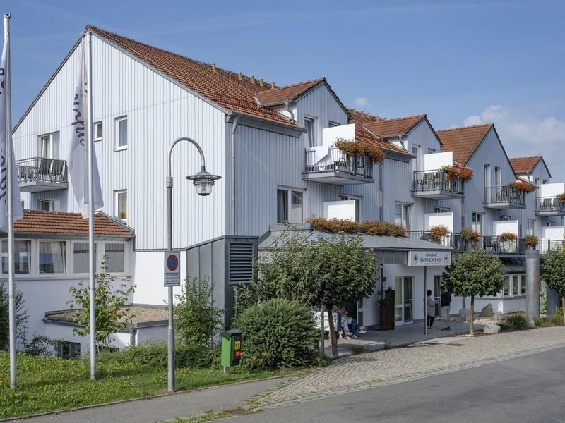 Edificio bianco dell'hotel con balconi e tetto in tegole marroni sotto un cielo azzurro.
