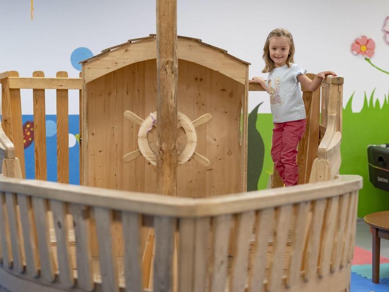 Bambino che gioca su un'area giochi interna a tema nave in legno con pareti colorate.