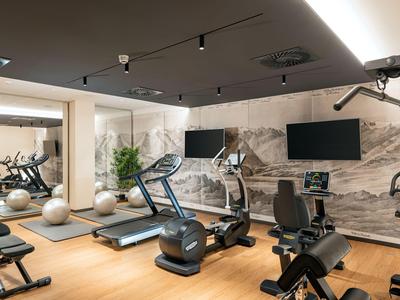 Moderner Fitnessraum mit verschiedenen Trainingsgeräten und großen Spiegeln an der Wand.