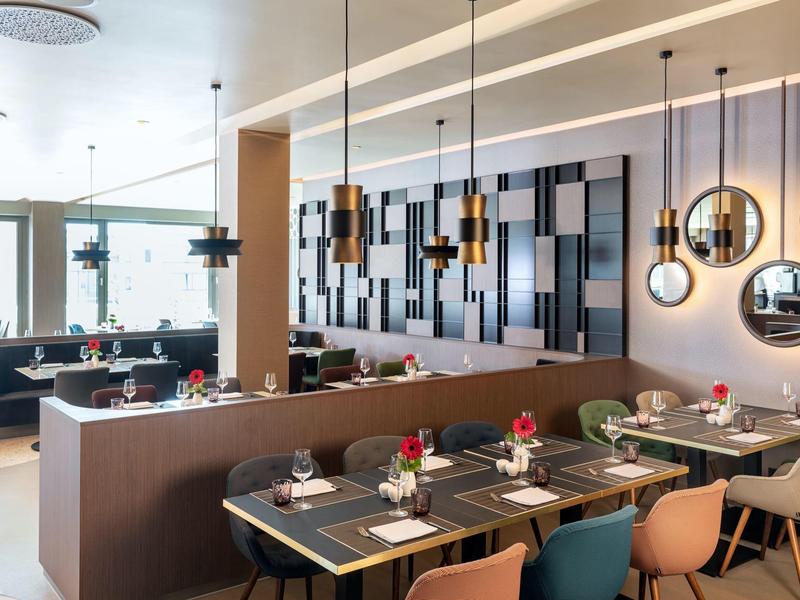 Nowoczesna restauracja hotelowa z stylowymi stołami, krzesłami i dekoracyjnymi lustrami na ścianie.