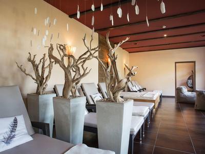 Moderner Innenraum mit weißen Stühlen, kahlen Bäumen in Töpfen und dunklem Holzboden.