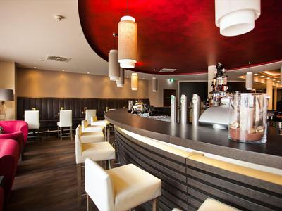 Moderner Hotelbarbereich mit weiß gepolsterten Barhockern und warmem Umgebungslicht.