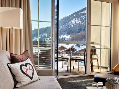 Modernes Wohnzimmer mit Glasfenstern und Blick auf verschneite Berge und Dorfhäuser.