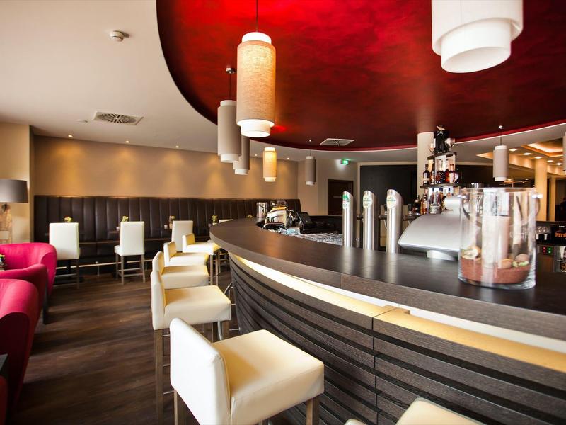 Moderne Bar mit weißem Tresen, roten Stühlen und Decke, braunem Holzboden, warm beleuchtet.