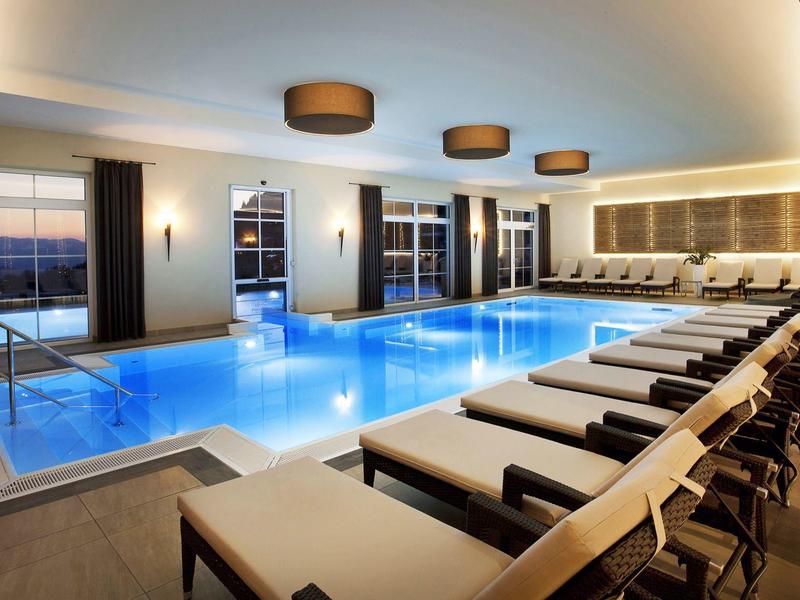 Helles Hallenbad mit Liegestühlen und großen Fenstern, die Tageslicht und Aussicht bieten.