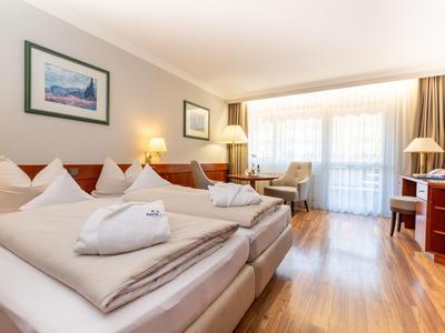 Lichte hotelkamer met twee bedden, houten vloer en balkon met uitzicht naar buiten.