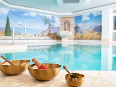 Una piscina coperta con acqua turchese, murales dipinti e tre ciotole sonore in primo piano.