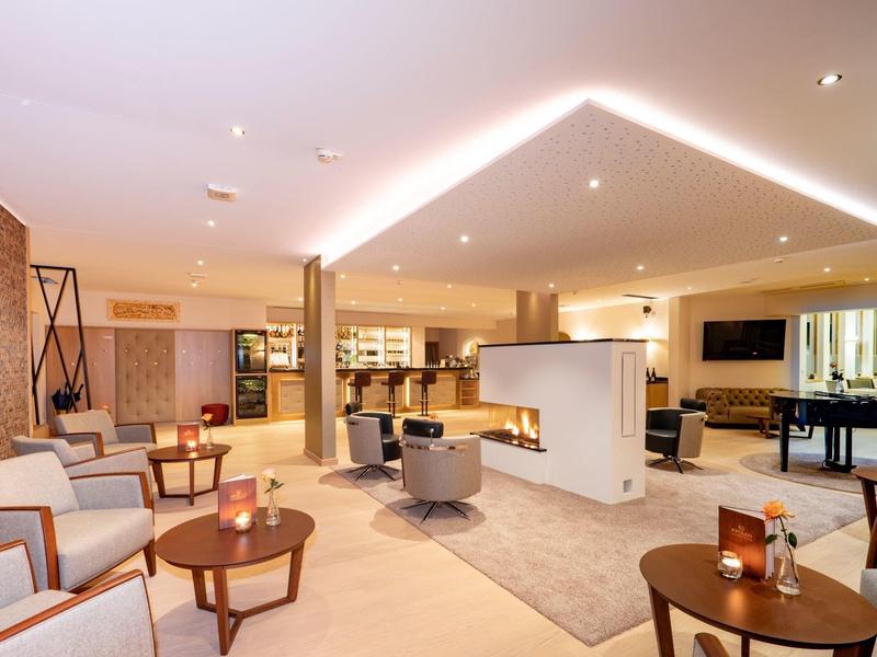 Hall di hotel moderno con aree salotto accoglienti, tavoli in legno e illuminazione elegante.