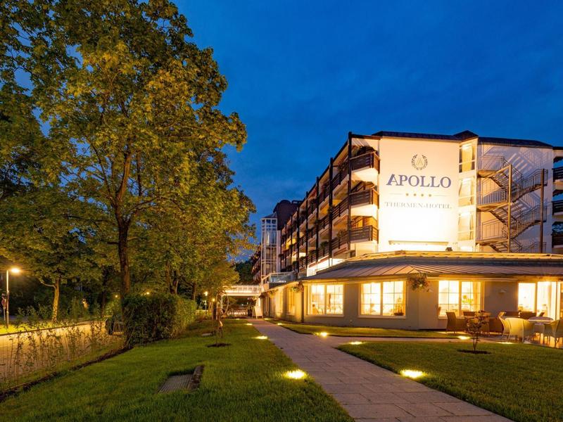 Hotel Apollo al crepuscolo con edificio illuminato e sentiero in primo piano.