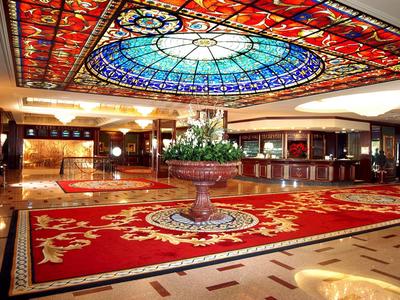 Luxuriöse Hotellobby mit prächtigem Teppich und bunt verglasster Decke.