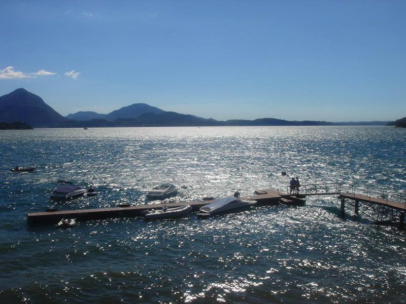 Zonnig meer met berglandschap en steiger, iemand staat op de steiger.