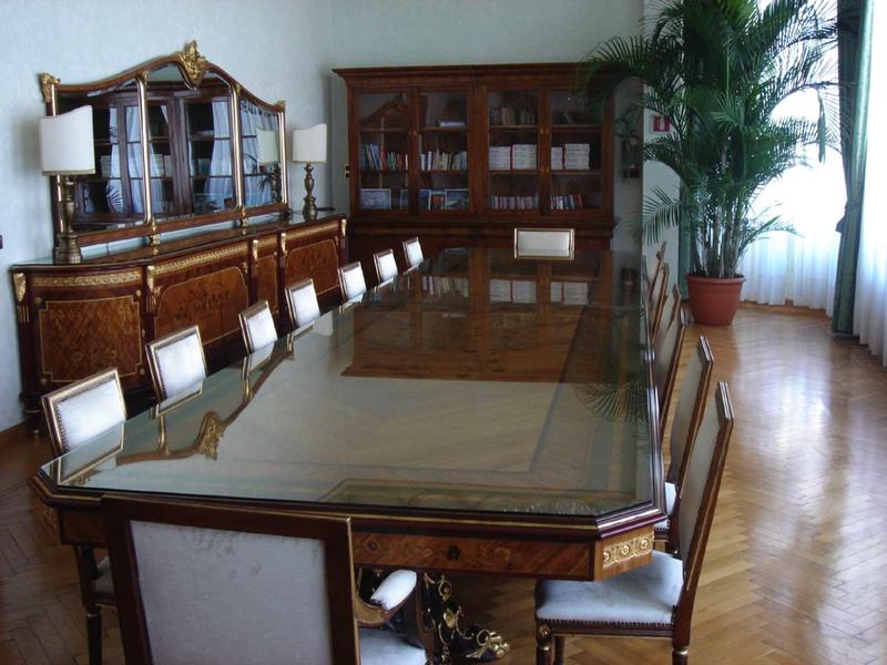 Elegant large wooden table with glass top and upholstered chairs in a classic dining room.