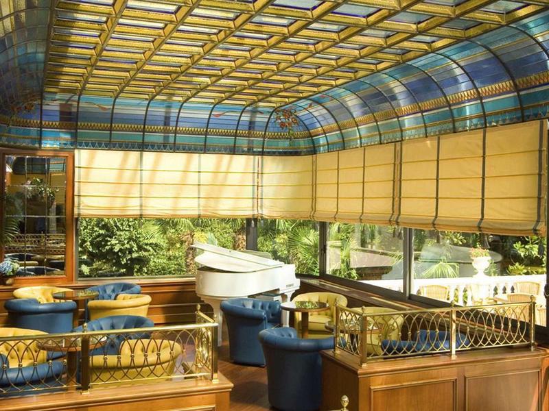 Elegant indoor area with blue armchairs, glass roof, abundant daylight and green outdoor view.