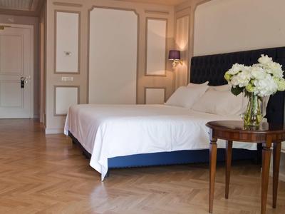 Elegantes Hotelzimmer mit Doppelbett, Holzboden und einem Beistelltisch mit weißem Blumenstrauß.