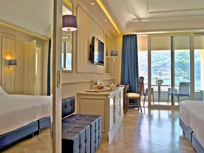 Helles Hotelzimmer mit zwei Betten, Fernseher, Spiegel und Balkon mit Blick auf das Wasser.