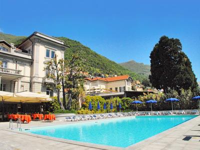 Ein Außenpool vor einem Hotel mit Bergen im Hintergrund und Sonnenschirmen am Pool.