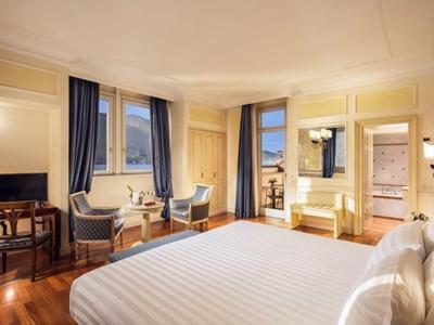 Camera d'hotel luminosa con letto grande, area salotto, TV e balcone con vista.