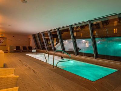 Piscina interna con illuminazione calda e grandi finestre in un hotel moderno.