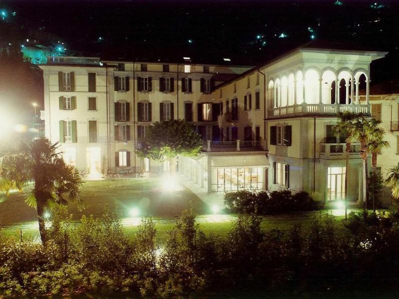 Edificio dell'hotel illuminato con giardino e alberi di notte.