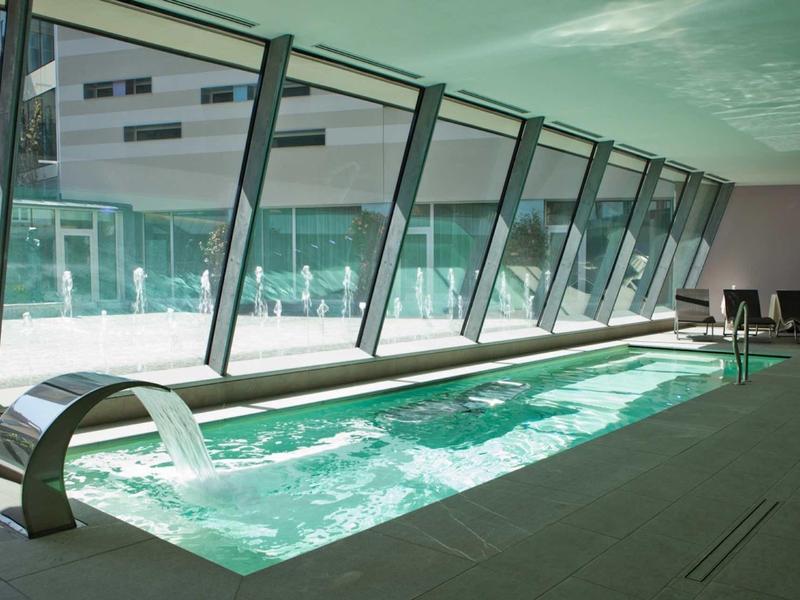 Piscina interna moderna con cascata e grandi finestre in una stanza luminosa