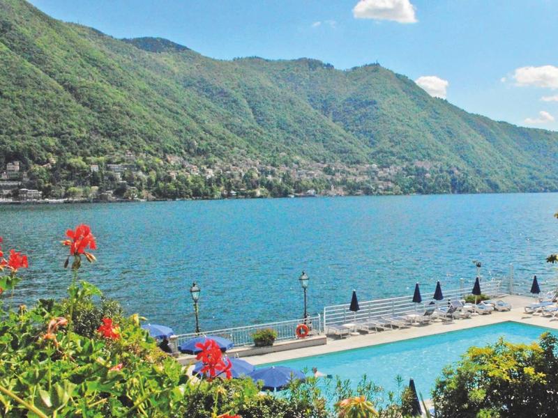 Vista su una piscina con un lago e montagne boschive sullo sfondo.