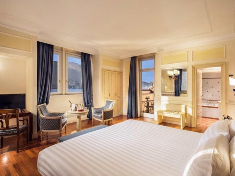 Camera d'hotel luminosa con letto grande, area salotto, TV e balcone con vista.