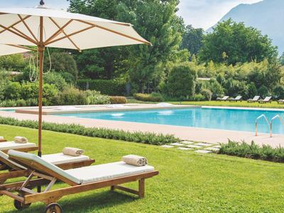 Sonnenliegen mit Handtüchern neben einem Pool und Sonnenschirm auf grünem Rasen.