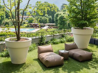 Gemütliche Sitzmöbel auf einer grasbewachsenen Terrasse neben großen Pflanzen in Töpfen.