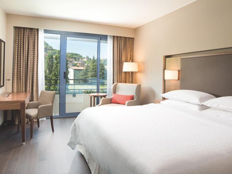 Moderne hotelkamer met tweepersoonsbedden, bureau, fauteuil en balkonzicht.