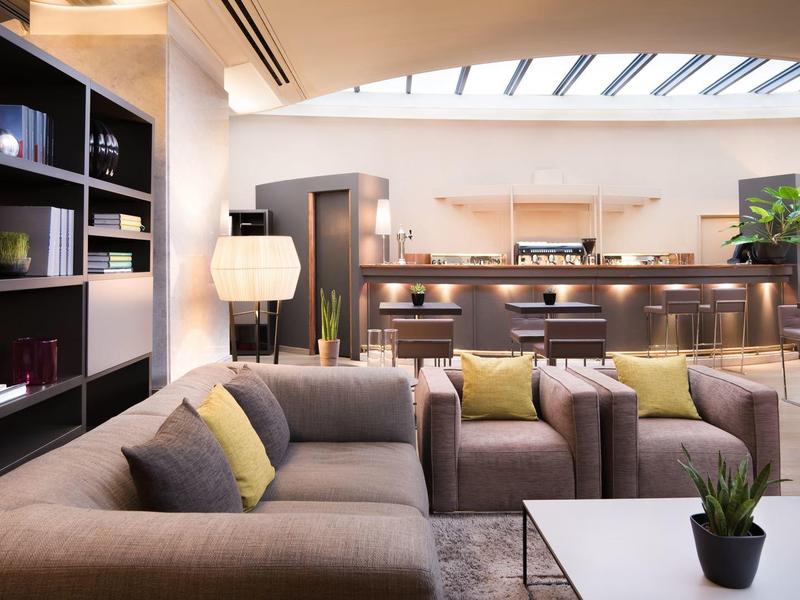 Modern ingerichte hotel lounge met comfortabele banken en verlichting onder een glazen dak.