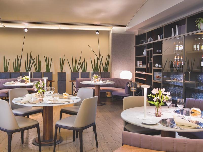 Elegant hotelrestaurant met ronde tafels, moderne inrichting en decoratieve planten.