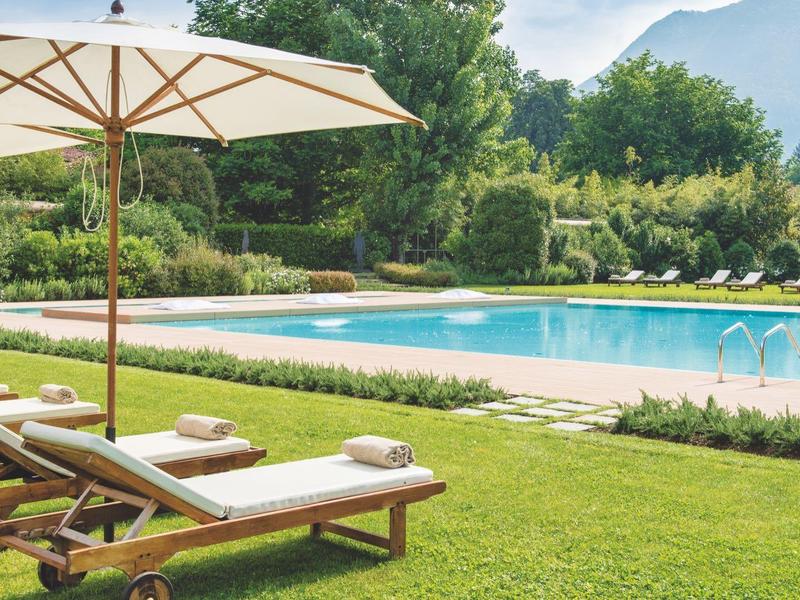 Zwembad met ligstoelen en parasol op groen gras in een rustige omgeving.