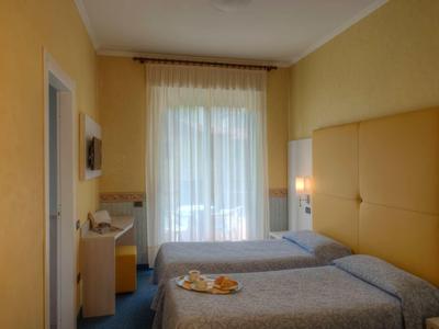 Hotelzimmer mit zwei Einzelbetten, gelben Wänden und einem Fenster mit weißen Vorhängen.