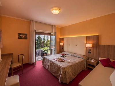 Hell eingerichtetes Hotelzimmer mit Doppelbett, Balkontür und Stuhl am Fenster.