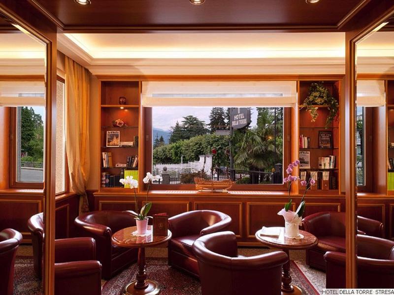 Accogliente area lounge dell'hotel con poltrone in pelle, tavoli e grande finestra con vista sul paesaggio verde.