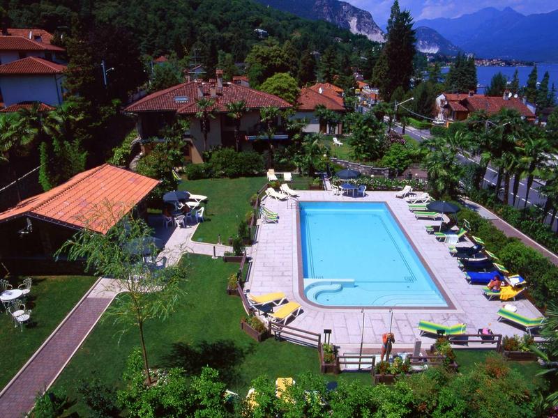 Vista di una piscina in un giardino con lettini e edifici circostanti davanti alle montagne.