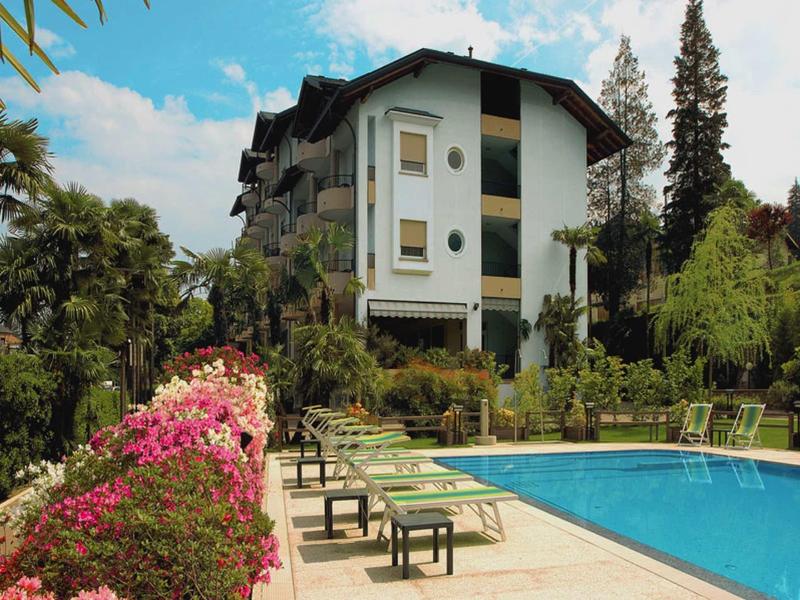 Hotel su più piani con piscina all'aperto e sedie a sdraio in un ambiente verde.