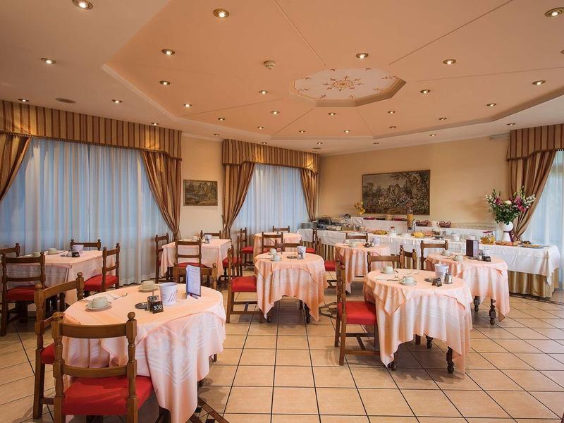 Elegante sala da pranzo con tavoli rotondi apparecchiati e sedie di legno rosse sotto luce calda.